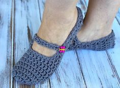 a woman's feet wearing gray crocheted slippers on top of a wooden floor