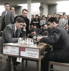 two men playing chess in front of a large group of people sitting at desks