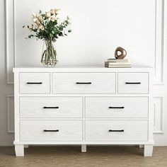 a white dresser with flowers in a vase on top and books sitting on the bottom