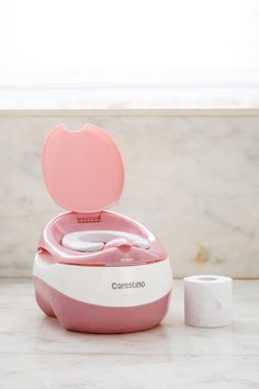 a pink and white baby potty sitting on top of a counter next to two rolls of toilet paper