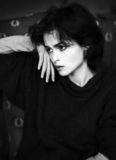 a black and white photo of a woman sitting on a couch with her hands behind her head