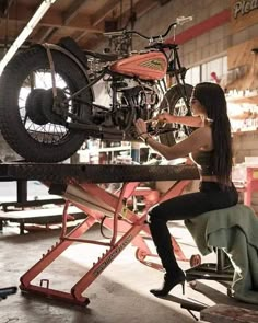 a woman sitting on a bench working on a motorcycle in a garage with other tools