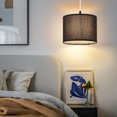 a lamp hanging over a bed next to a night stand and framed pictures on the wall