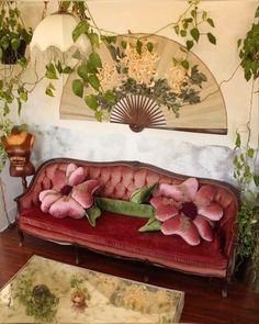 a red couch with pink flowers on it in front of a fan and other decorations