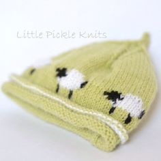 a green knitted hat with black sheep on it's side, sitting on a white surface