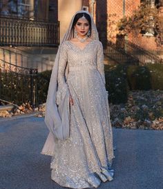 a woman in a silver gown and veil standing on the street with her hands behind her back