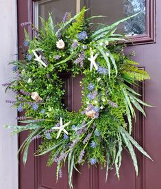 a wreath hanging on the front door of a house with purple flowers and greenery