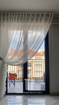 an open window with white sheer curtains and a red chair in the corner next to it