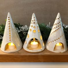 three white ceramic candlesticks sitting on top of a wooden shelf next to christmas greenery