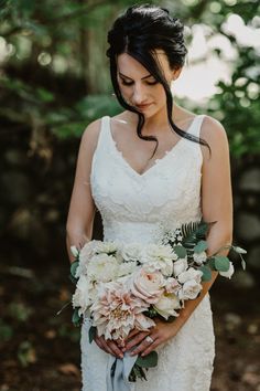 a woman in a wedding dress holding a bouquet of white and pink flowers with greenery