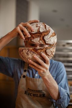 a man holding a loaf of bread in front of his face while wearing an apron