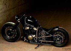 a black and gold motorcycle parked next to a green light in a dark room with concrete flooring