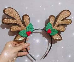 a hand holding up a mickey mouse ears headband with holly berry decorations on it