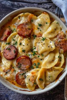 a white bowl filled with pasta and sausage on top of a table next to a fork