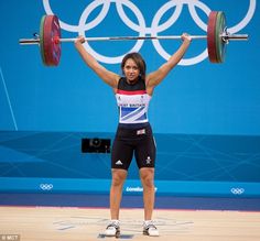 a woman lifting a barbell in front of the olympic logo