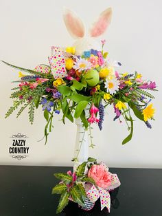 a vase filled with flowers and bunny ears on top of a black table next to a white wall