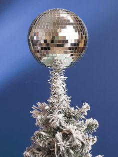 a silver disco ball sitting on top of a christmas tree covered in snow next to a blue sky