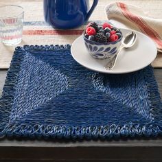 a bowl of berries and raspberries on a blue placemat with silverware