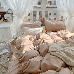 an unmade bed in front of a window with white curtains and pink comforter