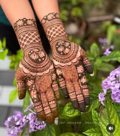 two hands with henna designs on them and purple flowers in the backgroud