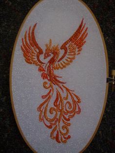 an embroidered wall hanging with a red and orange bird on it's left side