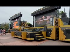 an outdoor stage set up with people walking around and onlookers in the background