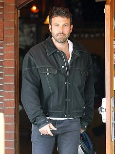 a man in black jacket and jeans standing at the door