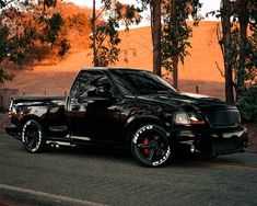 a black truck is parked on the side of the road in front of some trees