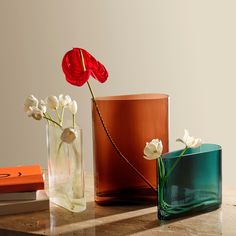 three vases with flowers in them sitting on a table next to books and magazines