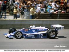 a man driving a racing car down a race track with people watching from the stands