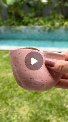 a person holding a pink cup in front of a swimming pool with green grass and trees