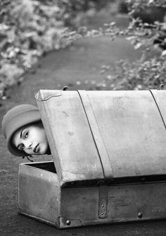 an old suitcase with a woman's face peeking out from it, sitting on the ground