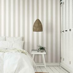 a bedroom with striped wallpaper and white bedding, along with a rattan lamp