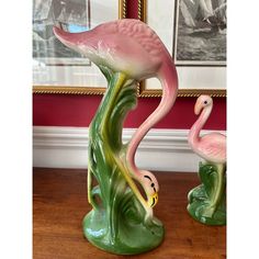 two pink flamingos sitting on top of a wooden table next to a framed photo