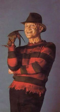 an old man wearing a striped shirt and hat holding a dead bird in his right hand