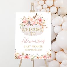 a welcome sign with flowers on it next to white balloons and a wooden easer