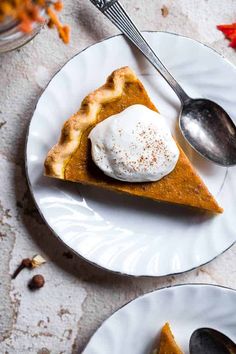 a slice of pumpkin pie with whipped cream on top and spoons next to it