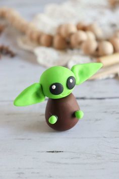 a small green toy sitting on top of a white wooden table next to beads and other items