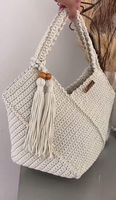 a white purse with tassels hanging from it's handle, and a hand holding