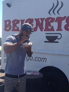 a man standing in front of a food truck eating something out of his hand while holding a hot dog