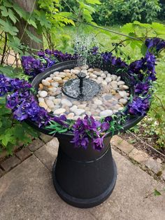 a bird bath with rocks and purple flowers