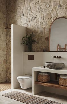 a white toilet sitting next to a sink in a bathroom under a mirror and a wooden shelf