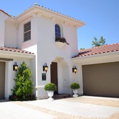 a large white house with two garages on each side and plants in the front