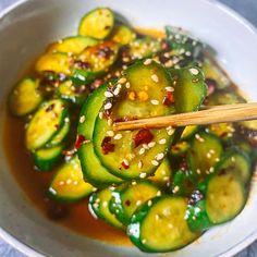 a white bowl filled with sliced cucumbers and sesame seeds, along with chopsticks