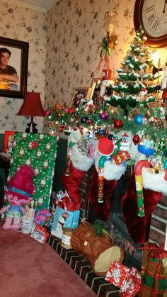 a christmas tree with presents under it in front of a clock and wallpapered walls