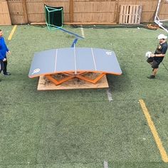 two people standing in the grass near a ping pong table