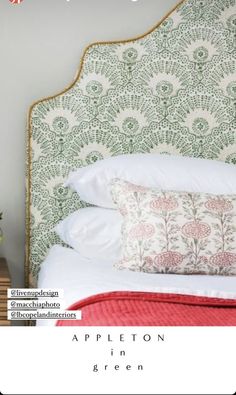 a bed with white pillows and green headboard next to a plant on a table