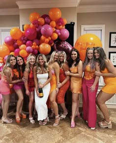 a group of women standing next to each other in front of balloons and oranges