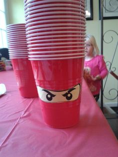 red cups with faces on them are sitting on a pink tablecloth at a children's birthday party