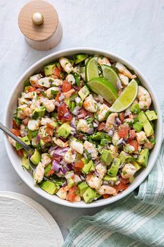 a white bowl filled with shrimp, avocado and red onion salad next to a wooden spoon